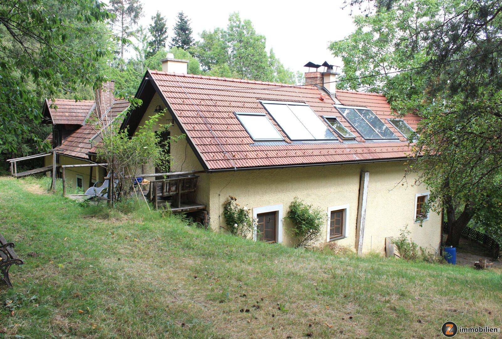 Rückansicht des Landhauses mit Ziegeldach, Dachfenstern und umgebender Natur.