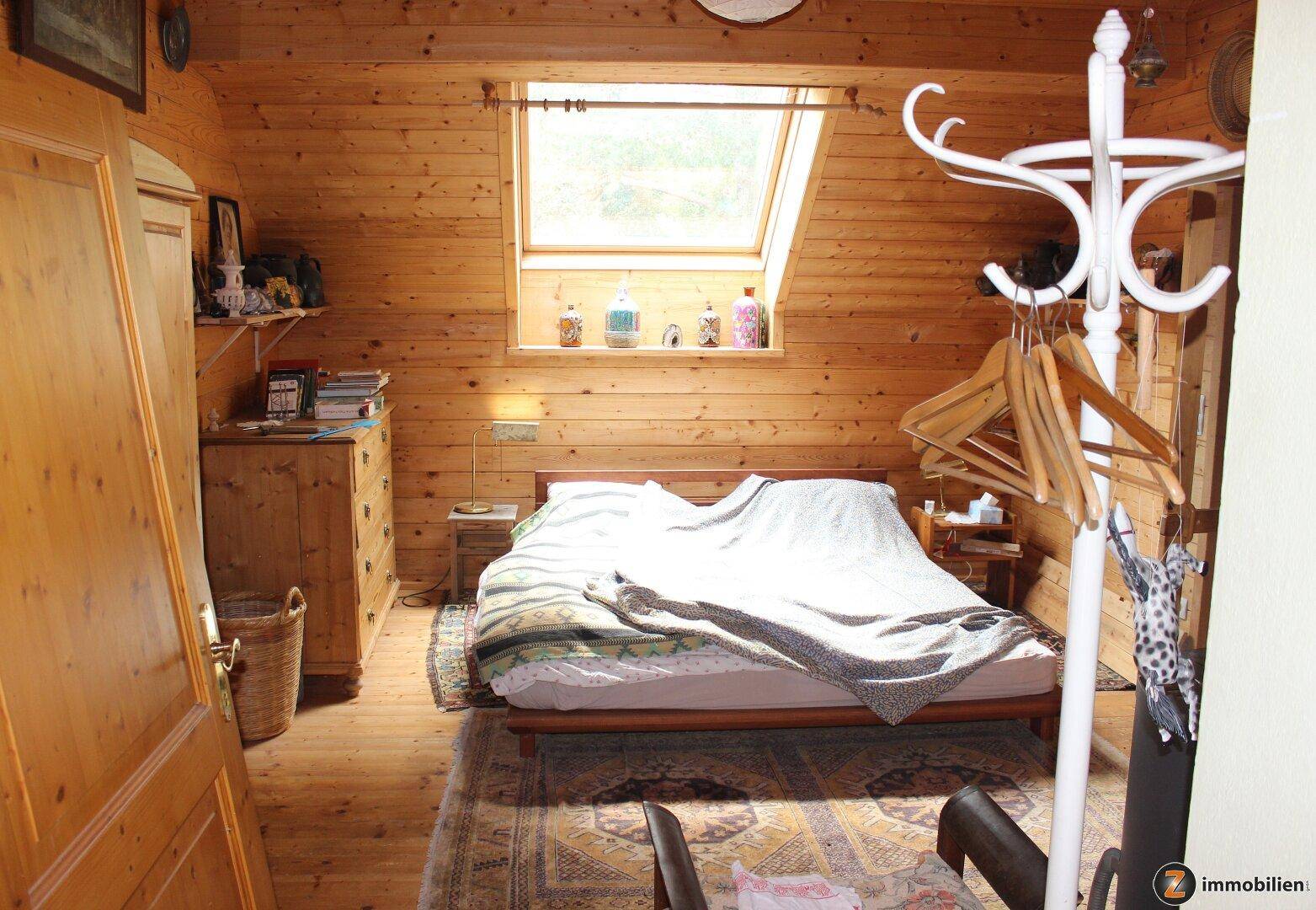 Helles Schlafzimmer mit Holzverkleidung, Dachfenster und einfacher Einrichtung.