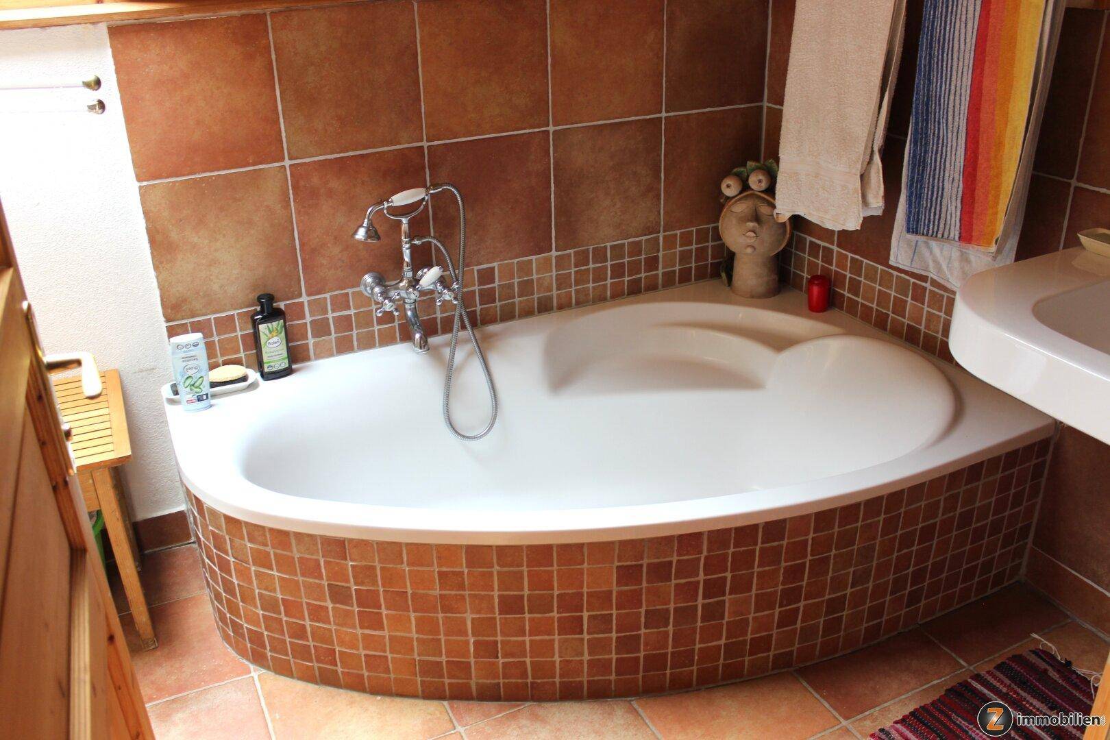 Badezimmer mit Eckbadewanne und braunen Fliesen, im traditionellen Stil gehalten.