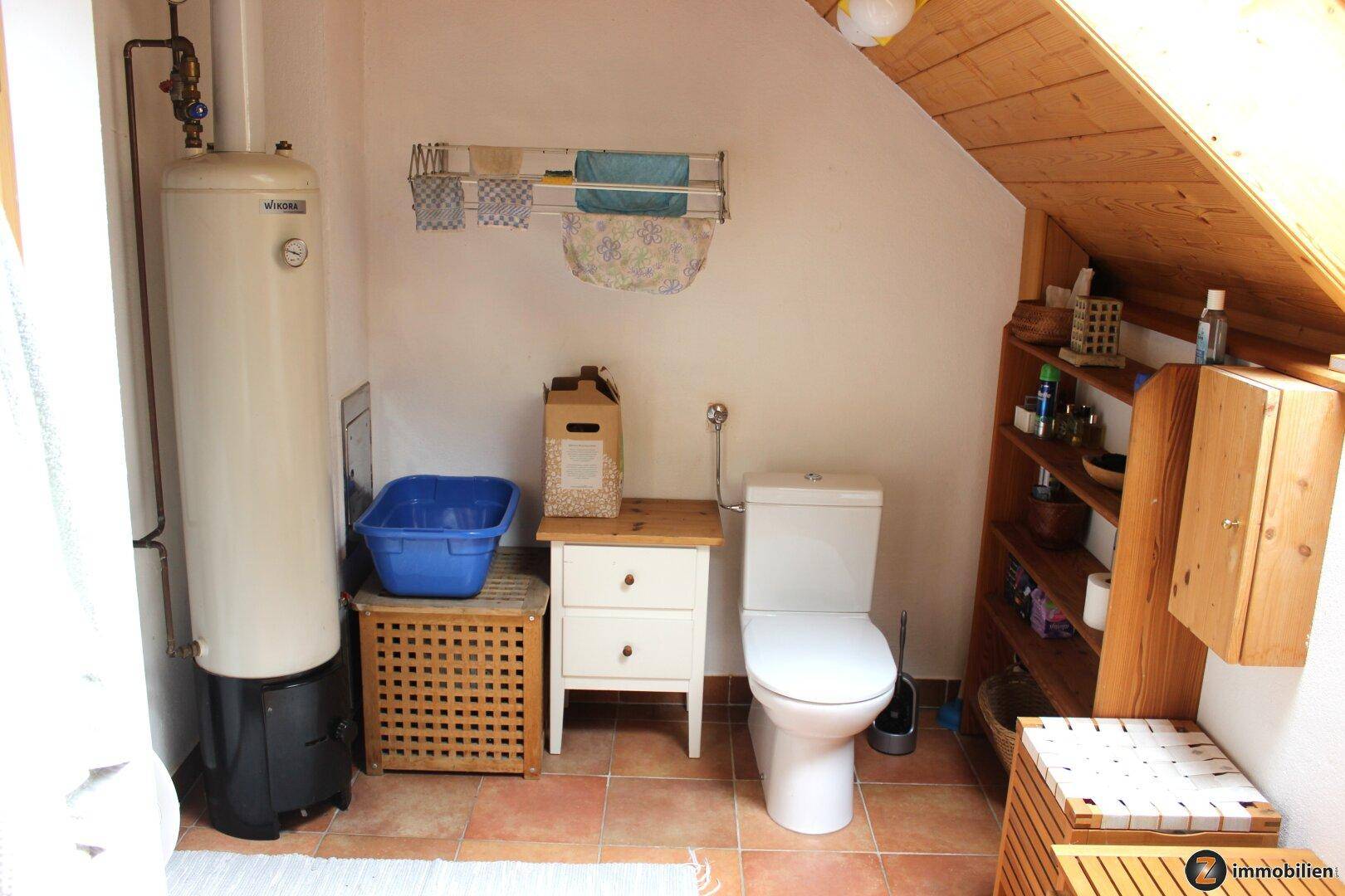 Kleiner Toilettenraum mit Warmwasserboiler, Fliesenboden und Dachschräge.