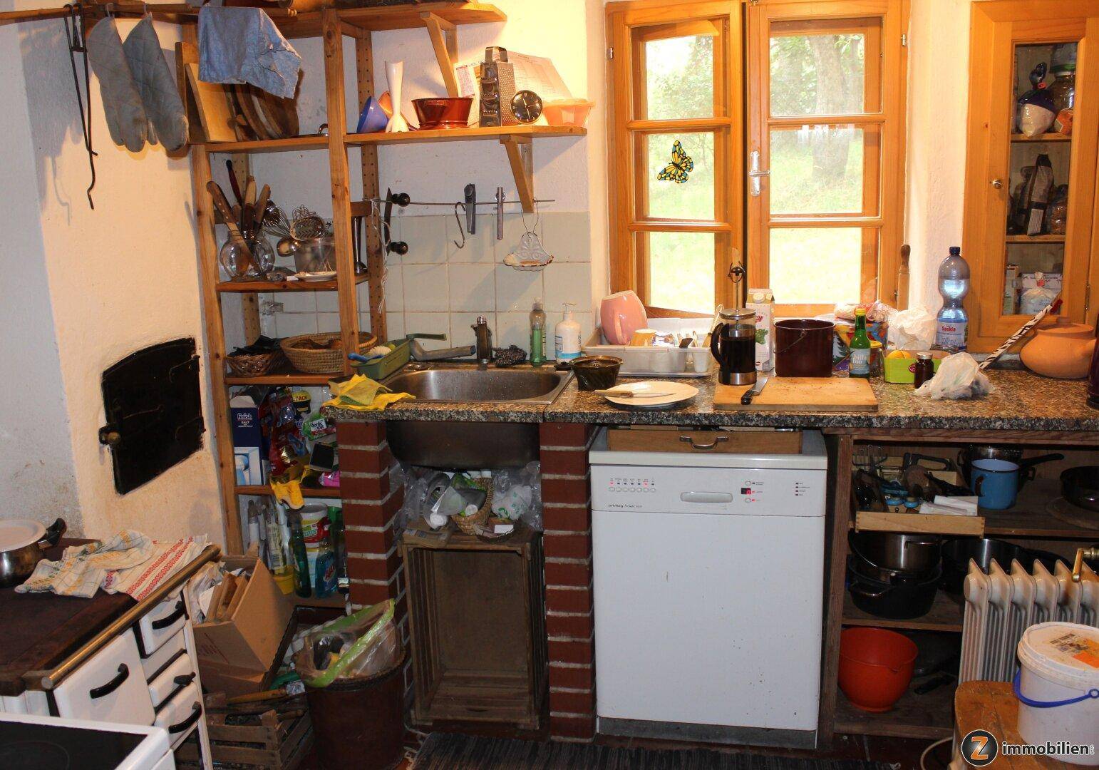 Rustikale Küche mit Spülbecken, Geschirrspüler und Holzregalen, mit Blick ins Grüne.