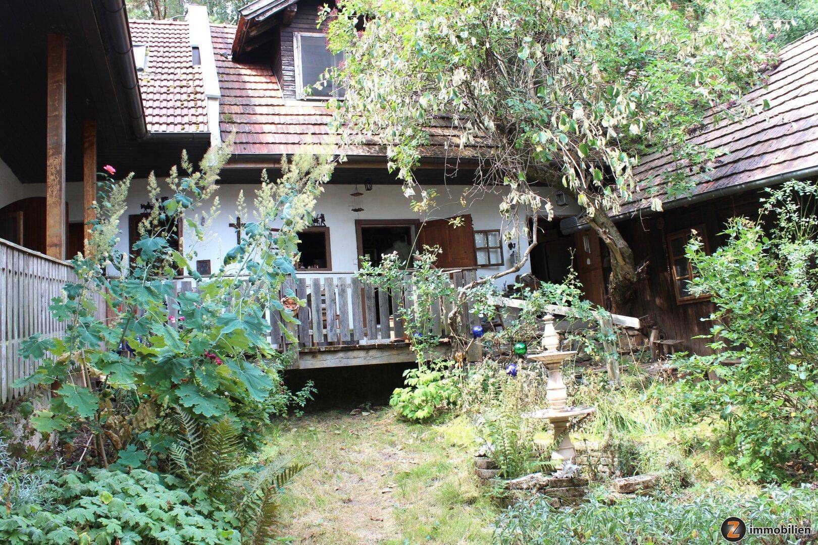 Rustikales Landhaus mit Holzterrasse und Geländer, umgeben von üppiger Vegetation.