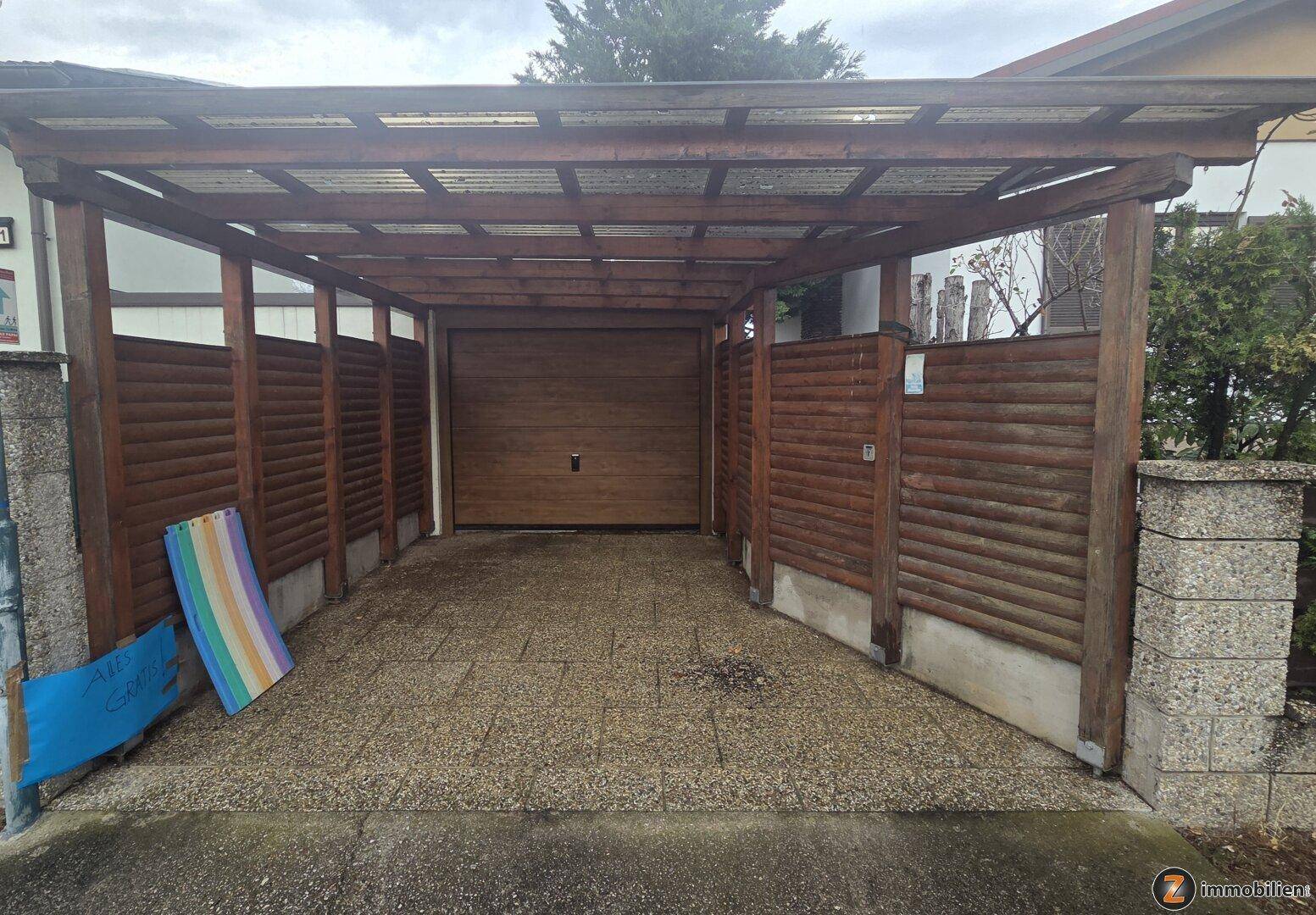 Überdachter Stellplatz mit Holzkonstruktion und Garagentor für Fahrzeuge.