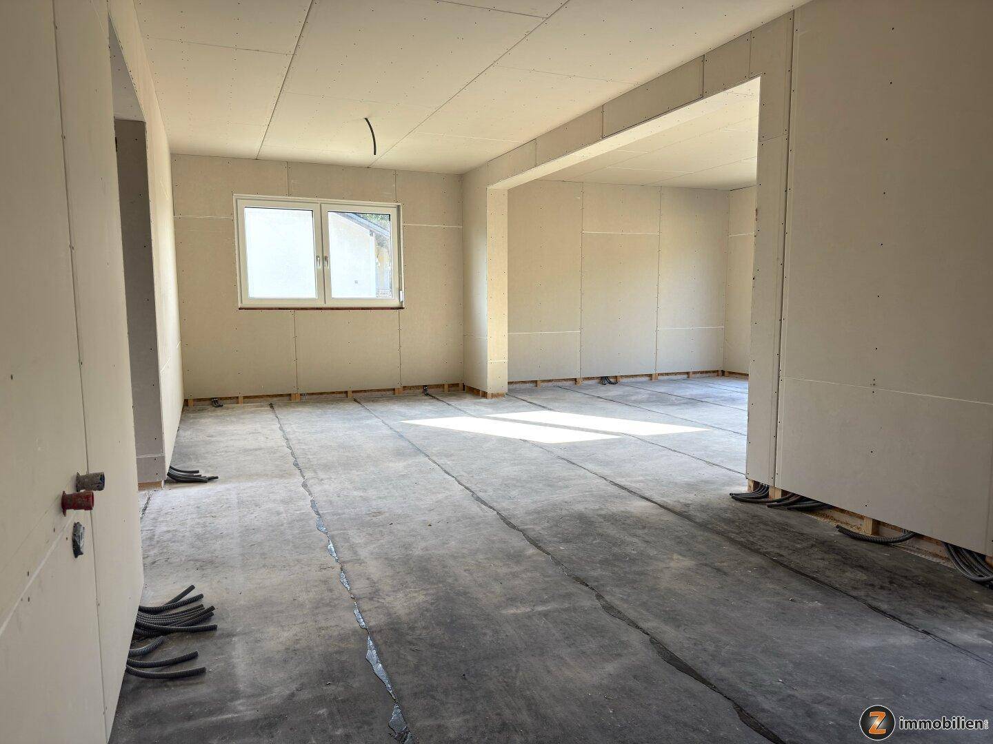 Großer offener Rohbaubereich mit Trockenbauwänden, Betonboden und mehreren Fensteröffnungen.