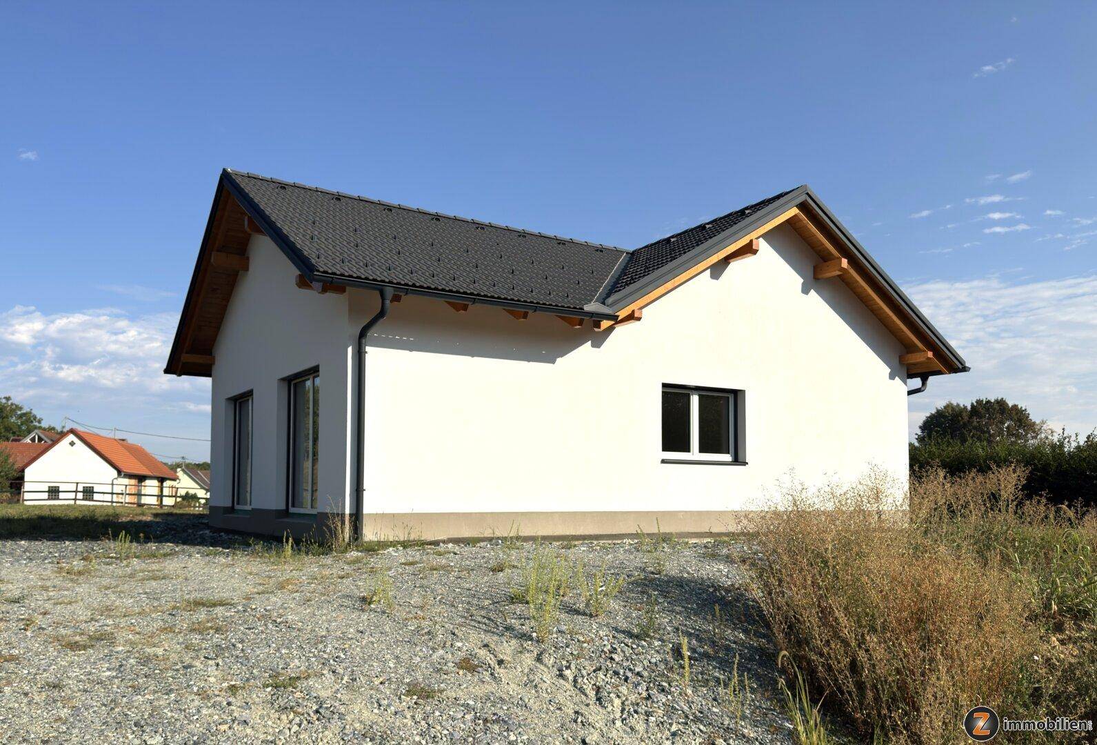 Rückansicht des Neubaus mit weißer Fassade, dunklem Dach und einfacher Gartengestaltung.