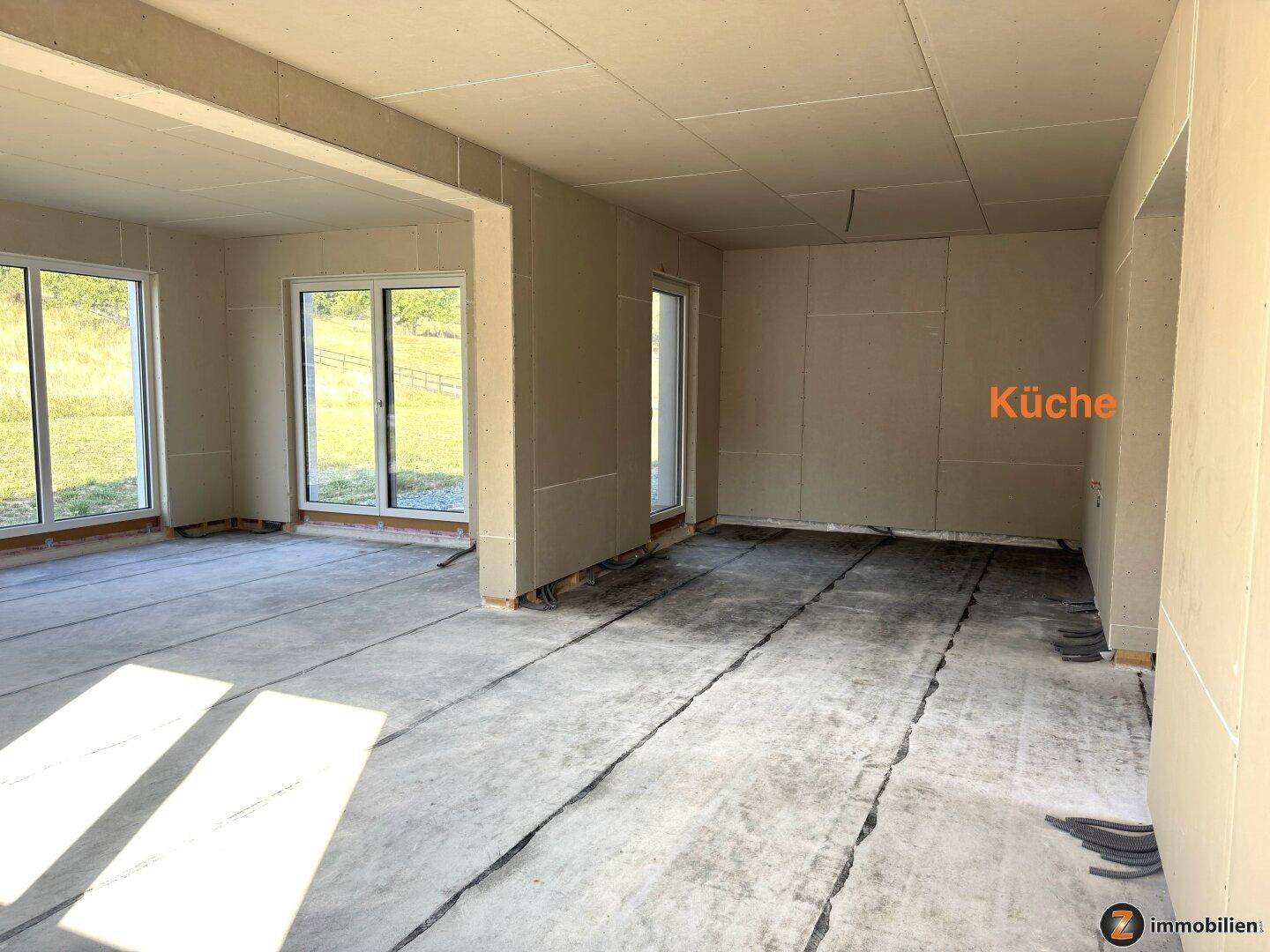 Offener Küchenbereich im Rohbau mit Trockenbauwänden und Betonboden, bereit für den Ausbau.