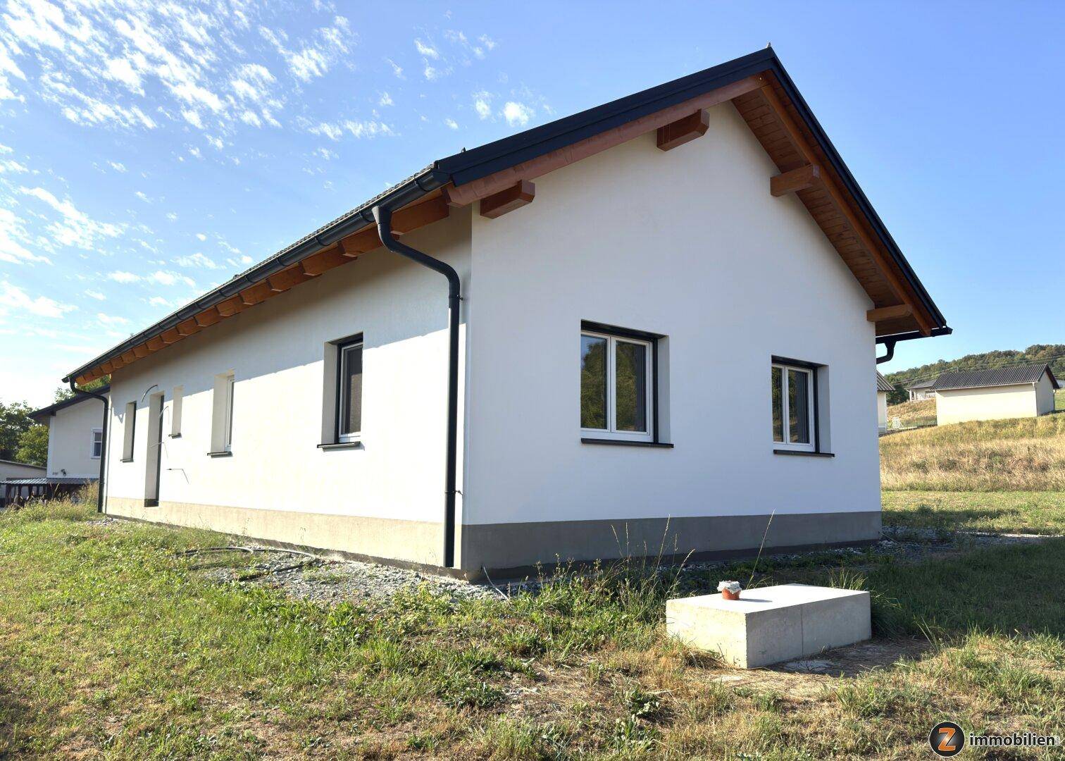 Seitenansicht des Neubaus mit weißer Fassade, dunklem Dach und sichtbaren Holzbalken.