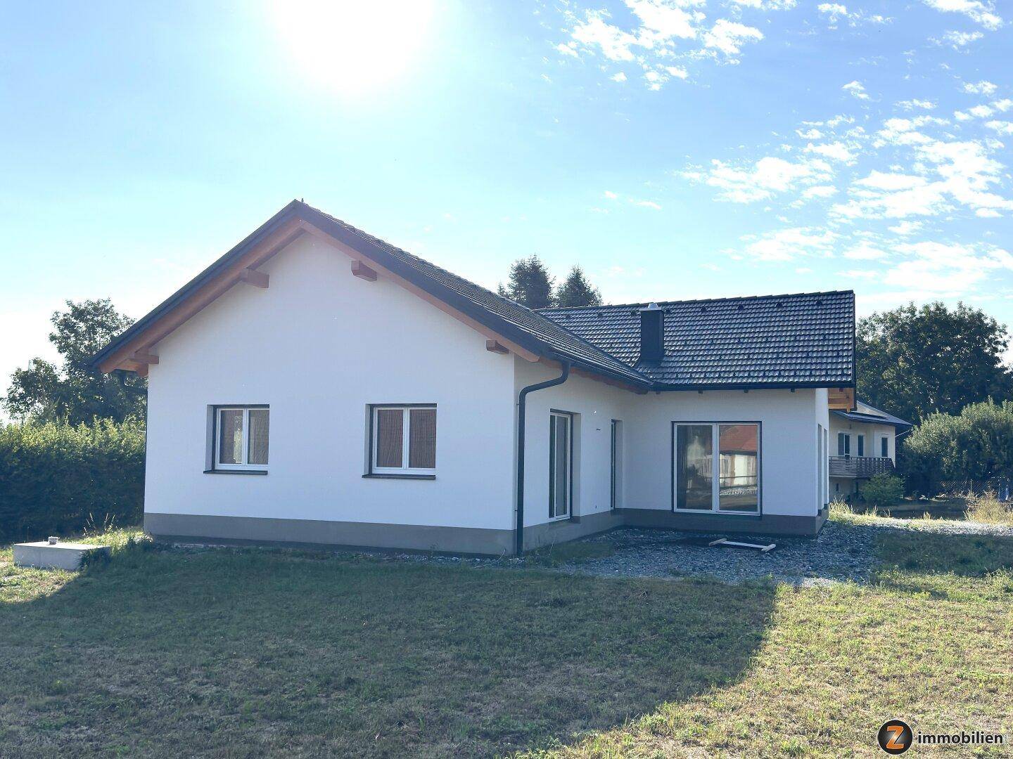 Neubau-Einfamilienhaus mit weißer Fassade und dunklem Satteldach in ländlicher Umgebung.