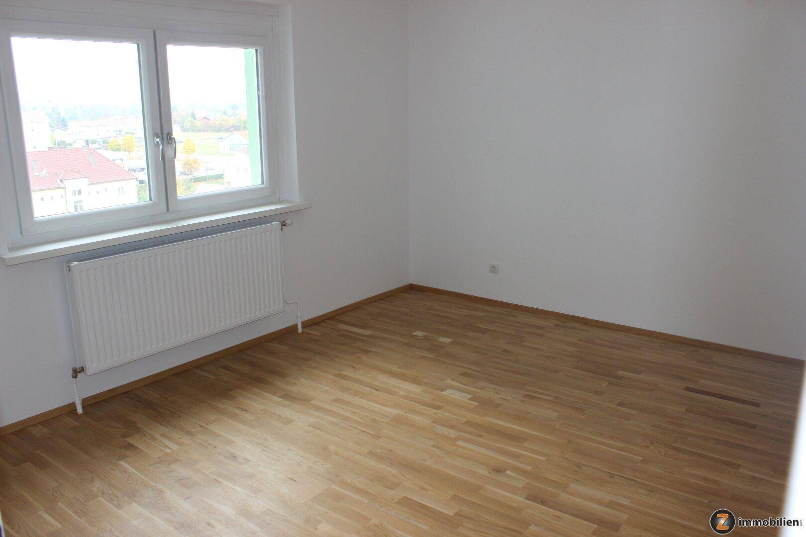 Helles Zimmer mit Parkettboden und großem Fenster, das einen Ausblick auf die Umgebung bietet.