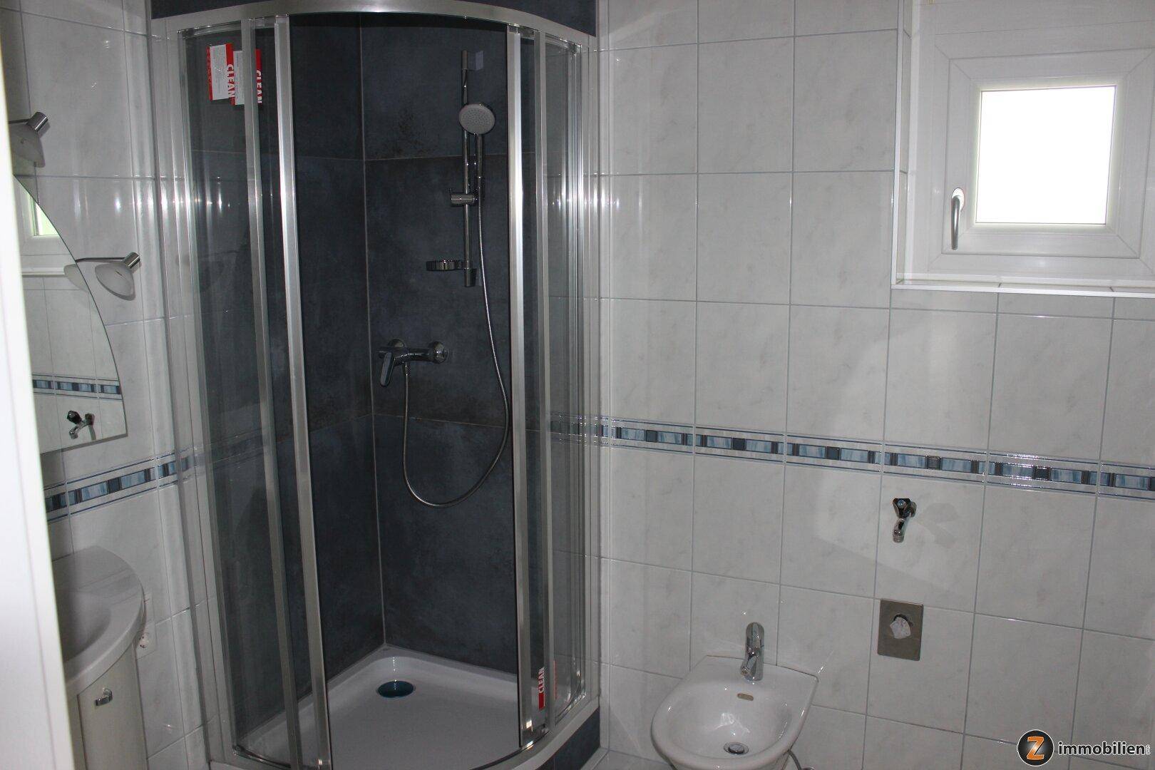 Badezimmer mit Eckduschkabine, weißen Fliesen, blauem Dekor und einem Fenster für Tageslicht.