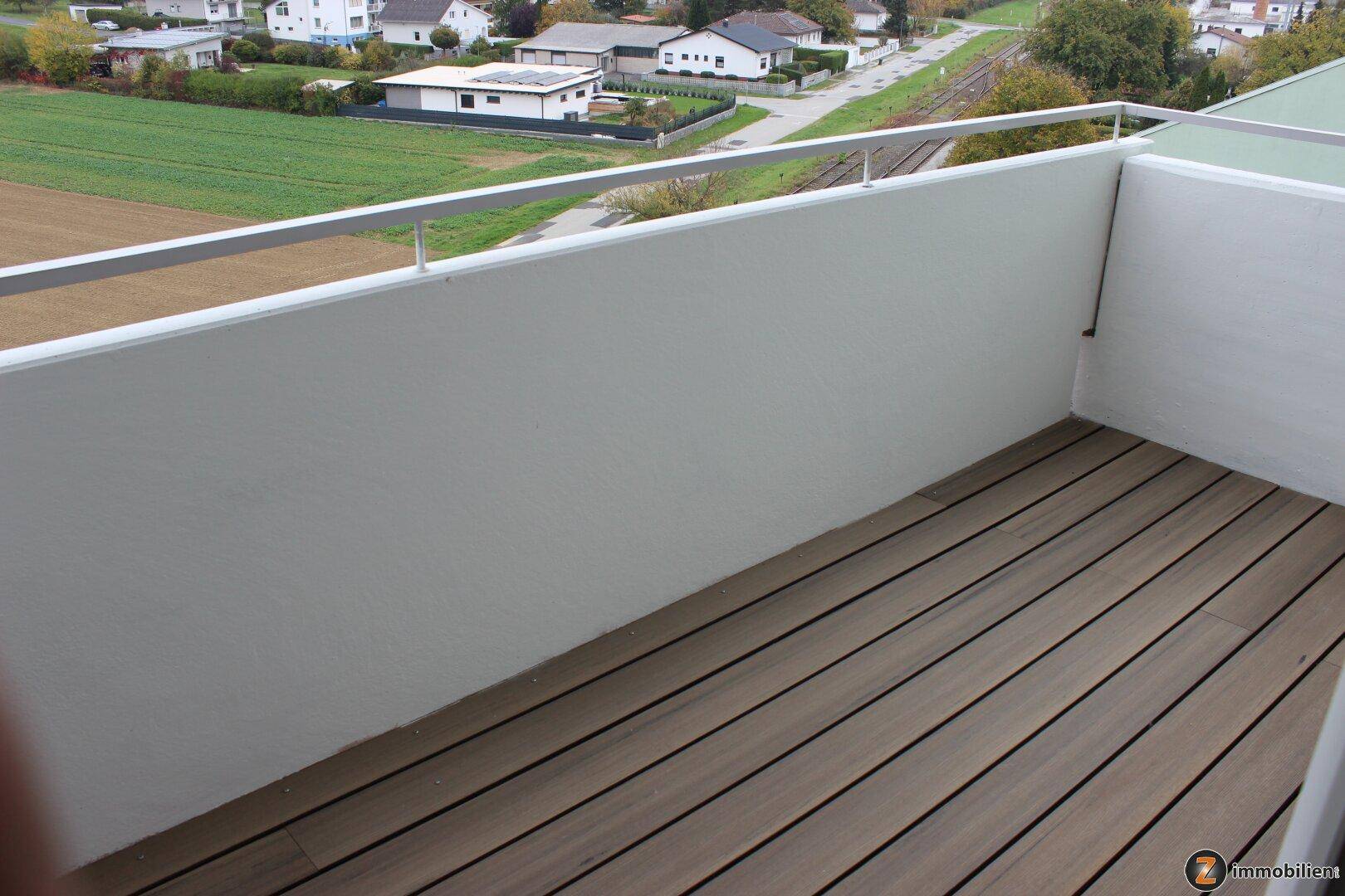 Balkon mit Holzdielen und weißem Geländer, bietet einen weiten Blick über die Landschaft.