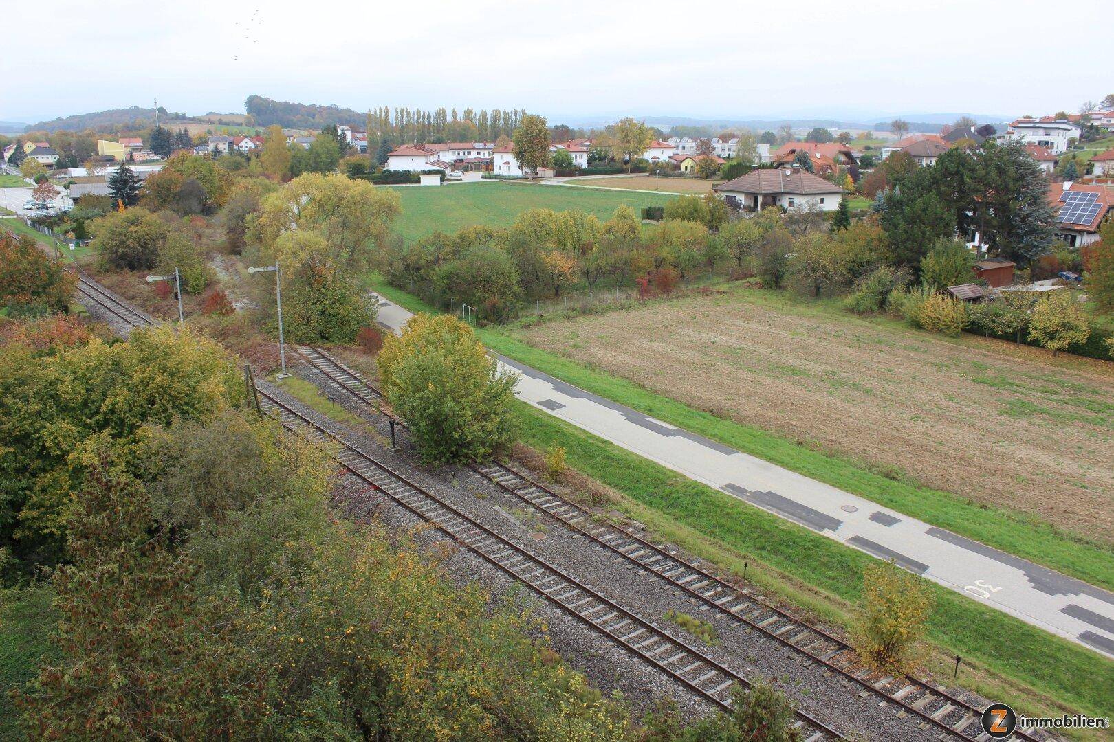 Weitläufiger Blick über eine ländliche Gegend mit Feldern, Häusern und Bahngleisen.