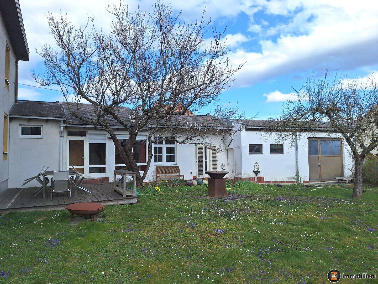 Großer Garten mit Rasenfläche, Bäumen und einer Holzterrasse.