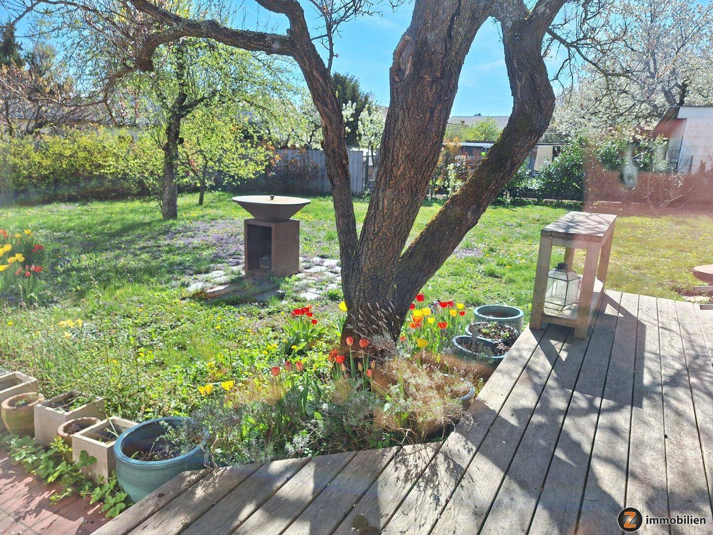 Gepflegter Garten mit blühenden Blumen, Bäumen und Holzterrasse.