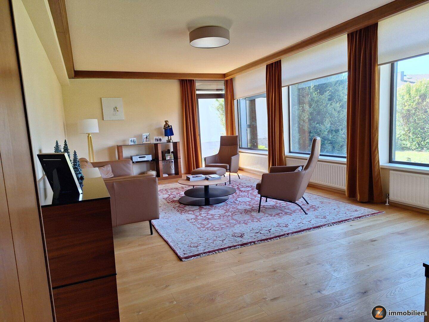 Geräumiges Wohnzimmer mit Holzbalken, großen Fenstern und hellem Parkettboden.
