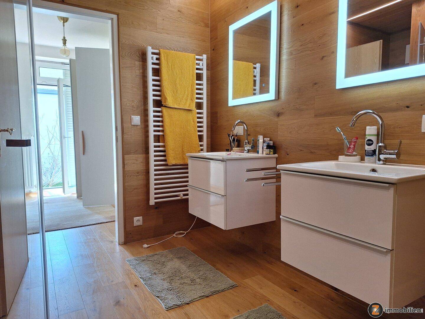 Modernes Badezimmer mit Doppelwaschbecken, Holzverkleidung und beheiztem Handtuchhalter.