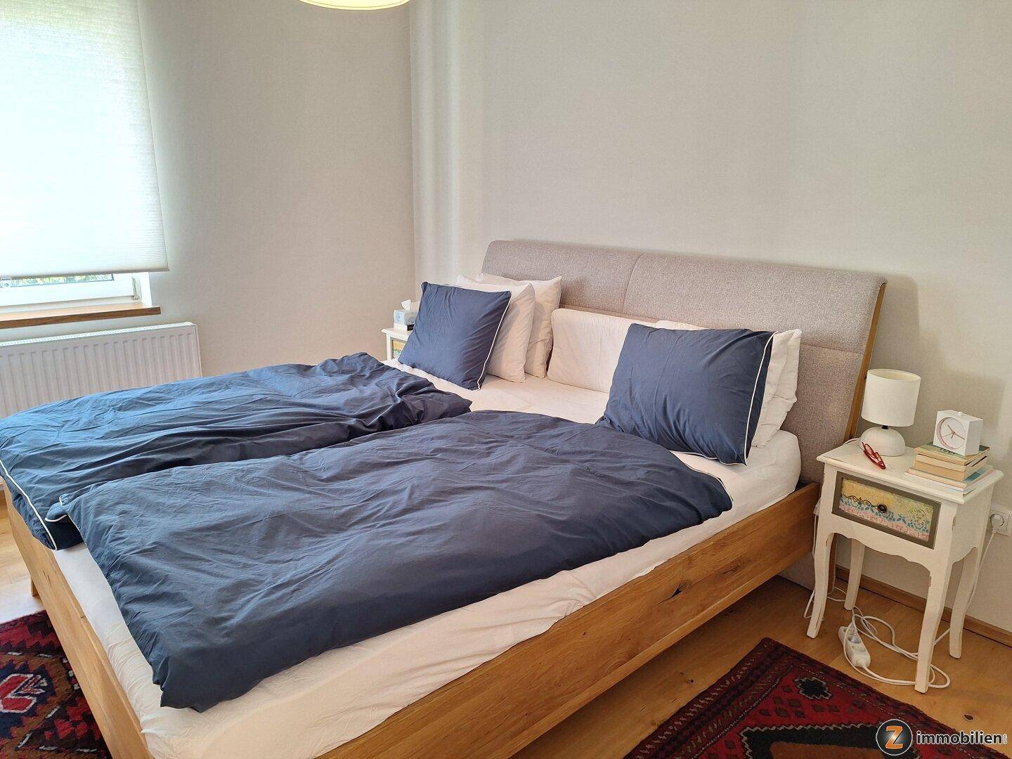 Helles Schlafzimmer mit Doppelbett, Holzboden und Fenster mit Rollladen.