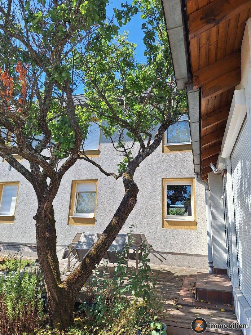 Seitenansicht des Hauses mit Bäumen und einer kleinen Terrasse.