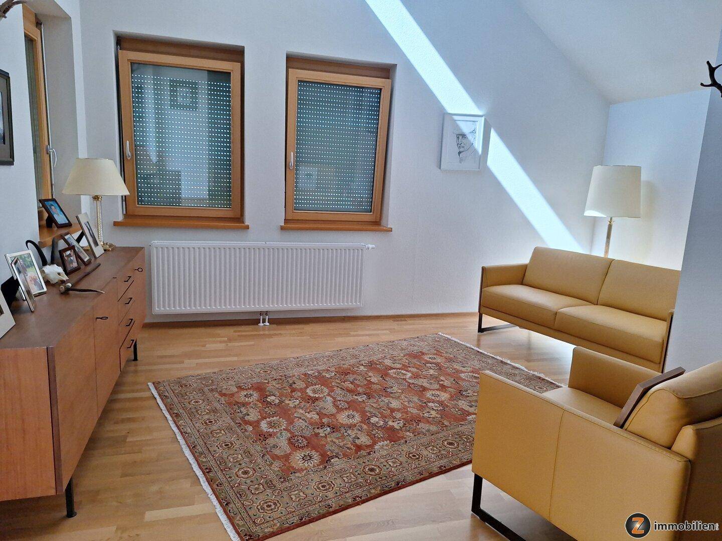 Gemütliches Wohnzimmer im Dachgeschoss mit Schrägen, Holzboden und bequemen Sofas.