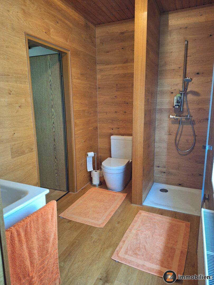 Badezimmer mit Holzwänden, ebenerdiger Dusche und wandhängendem WC.