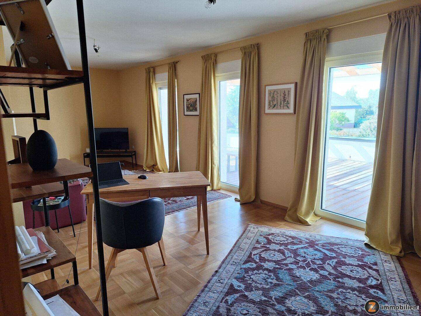 Helles Arbeitszimmer mit Holztisch, Teppich und Zugang zur Dachterrasse.