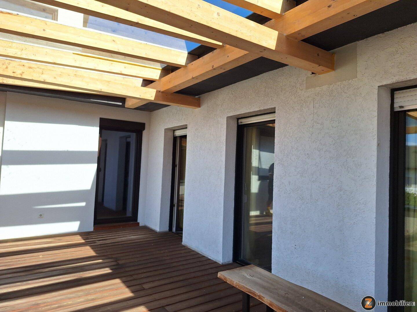 Große Holzterrasse mit Pergola und Zugang zu den Innenräumen.