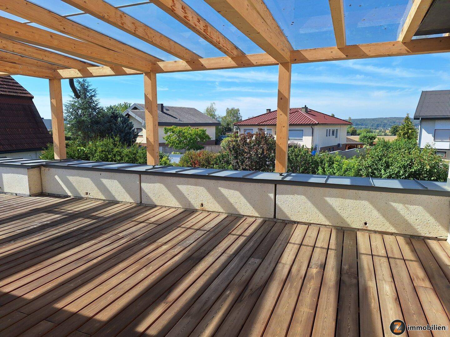 Geräumige Dachterrasse mit Holzbelag, Pergola und weitem Blick über die Umgebung.