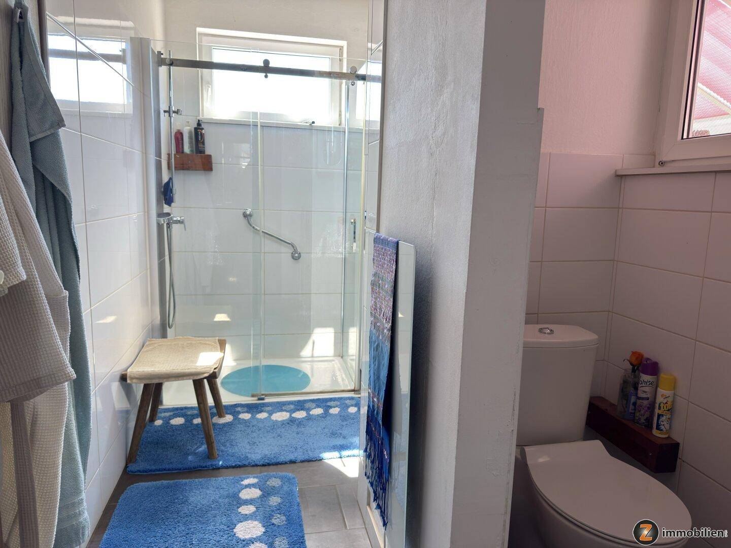 Modernes Badezimmer mit Duschkabine, WC und hellen Fliesen, ausgestattet mit Haltegriffen.