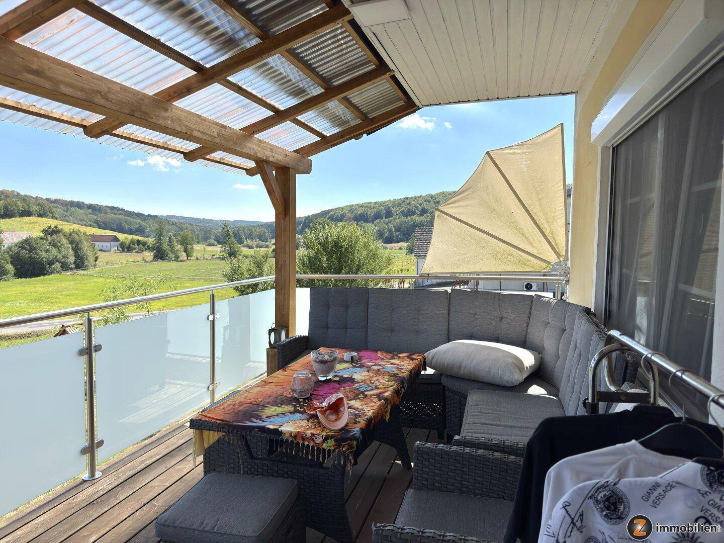 Überdachter Balkon mit Sitzgelegenheiten und weitem Blick über die grüne Landschaft.