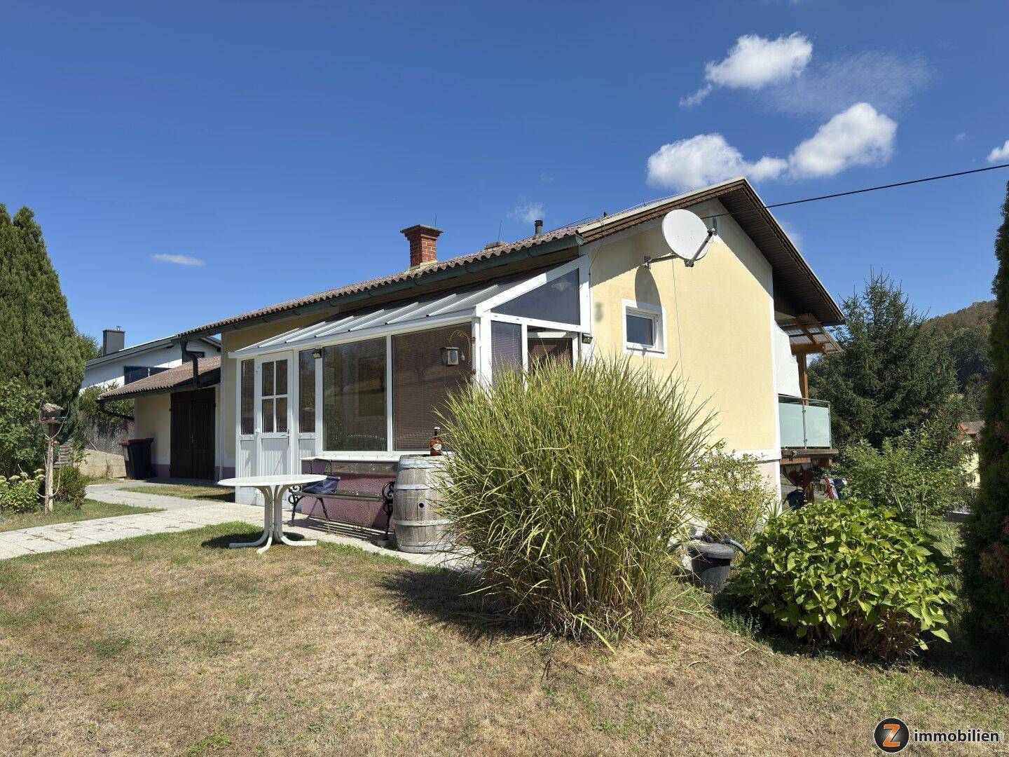 Seitenansicht des Hauses mit Wintergarten und gepflegtem Vorgarten an einem sonnigen Tag.