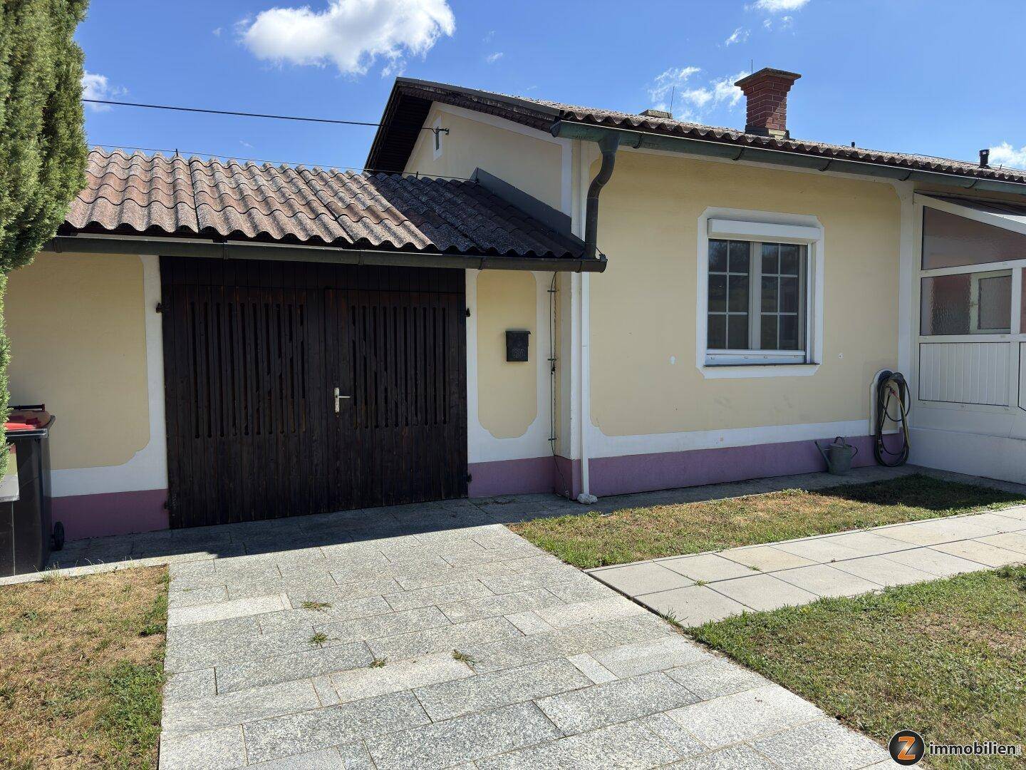 Seitenansicht des Hauses mit Garage und gepflasterter Zufahrt unter blauem Himmel.