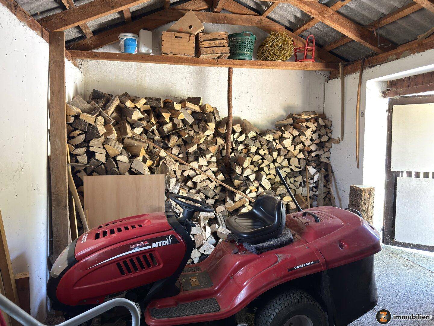 Geräteschuppen mit Holzstapel und Rasenmäher, ideal für die Lagerung von Gartengeräten.