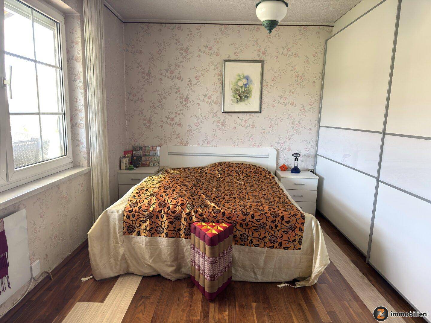 Schlafzimmer mit Doppelbett, Schiebetürenschrank und floraler Tapete, die eine gemütliche Atmosphäre schafft.