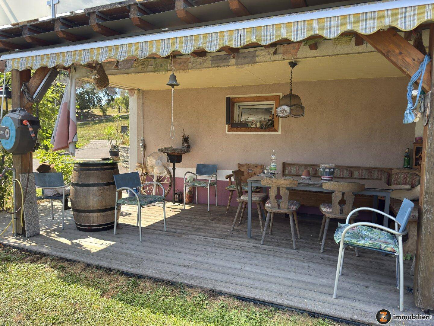 Überdachte Terrasse mit Holzboden, Sitzgelegenheiten und Blick ins Grüne, ideal zum Entspannen.