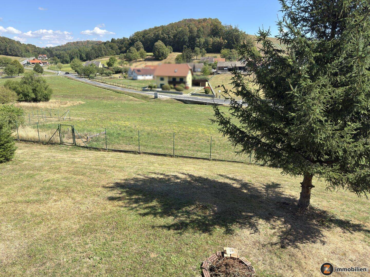 Weitläufige Rasenfläche mit Baum und Blick auf die umliegende Landschaft unter blauem Himmel.