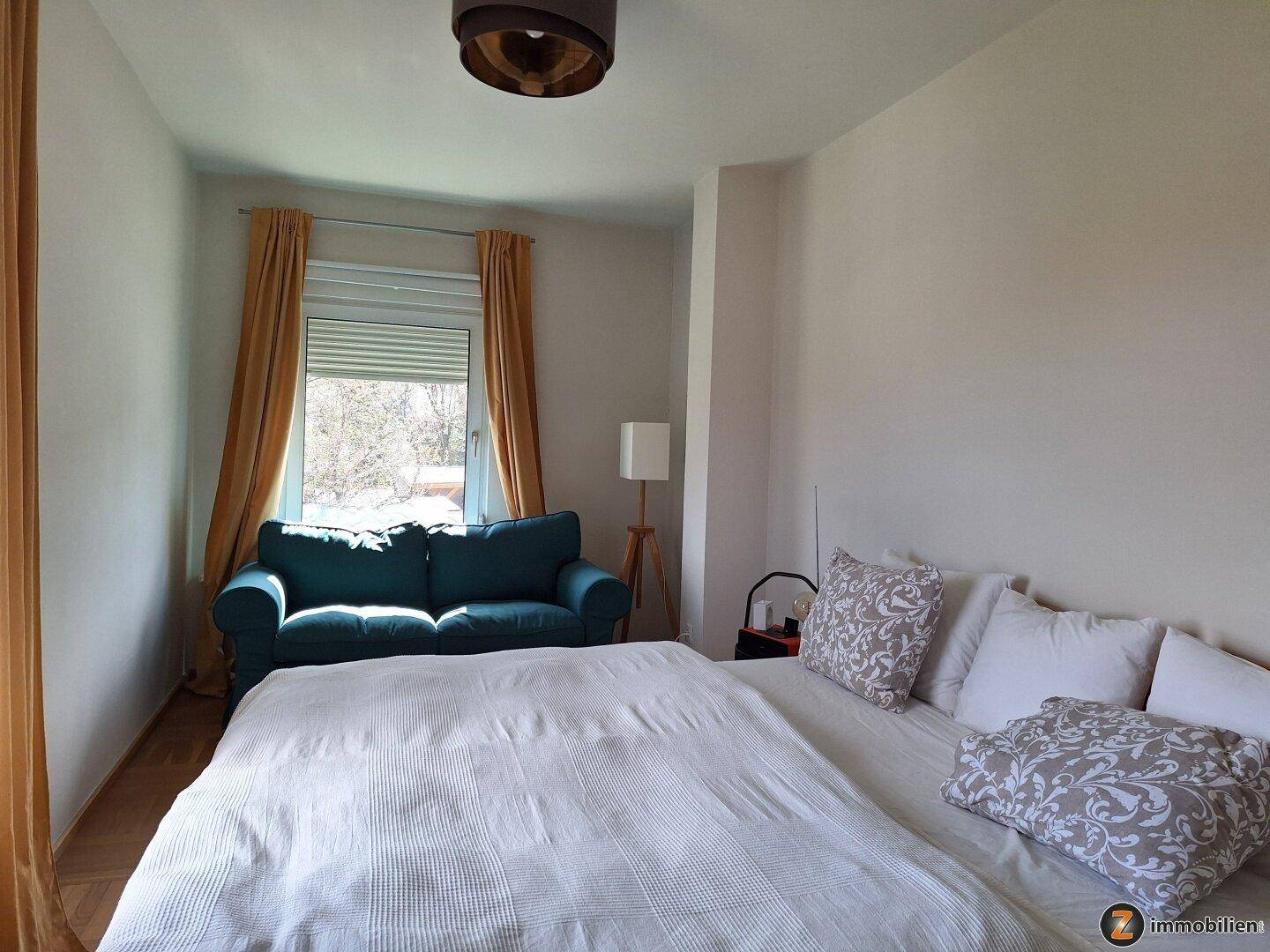 Schlafzimmer mit Doppelbett, Sofa und Fenster mit Rollladen.