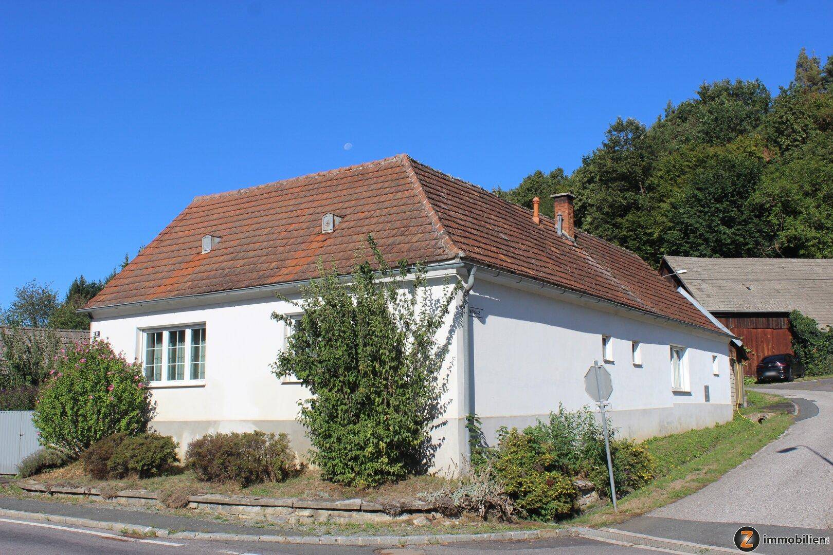 Seitenansicht des Hauses mit traditionellem Ziegeldach und umgebender Natur.
