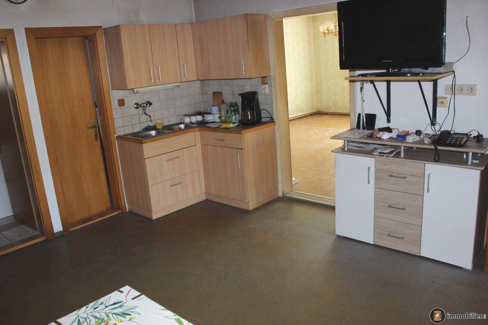 Einfache Küche mit hellen Holzschränken, Spüle und einem Fernseher auf einem Sideboard.
