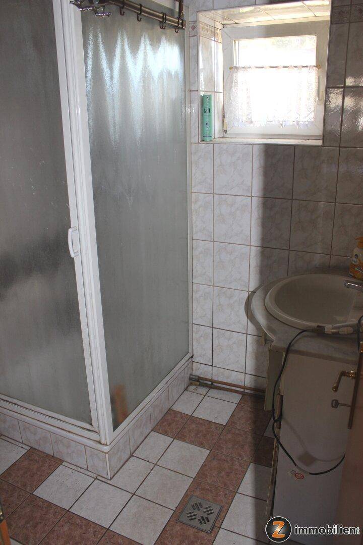 Badezimmer mit Duschkabine, Waschbecken und Fliesen an Wänden und Boden.