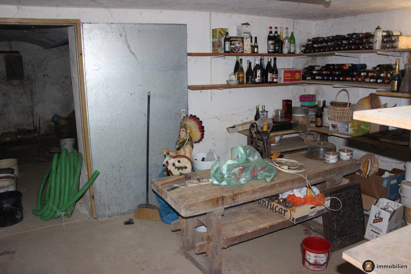 Kellerraum mit Regalen voller Flaschen, einer Werkbank und weiteren Lagerflächen.