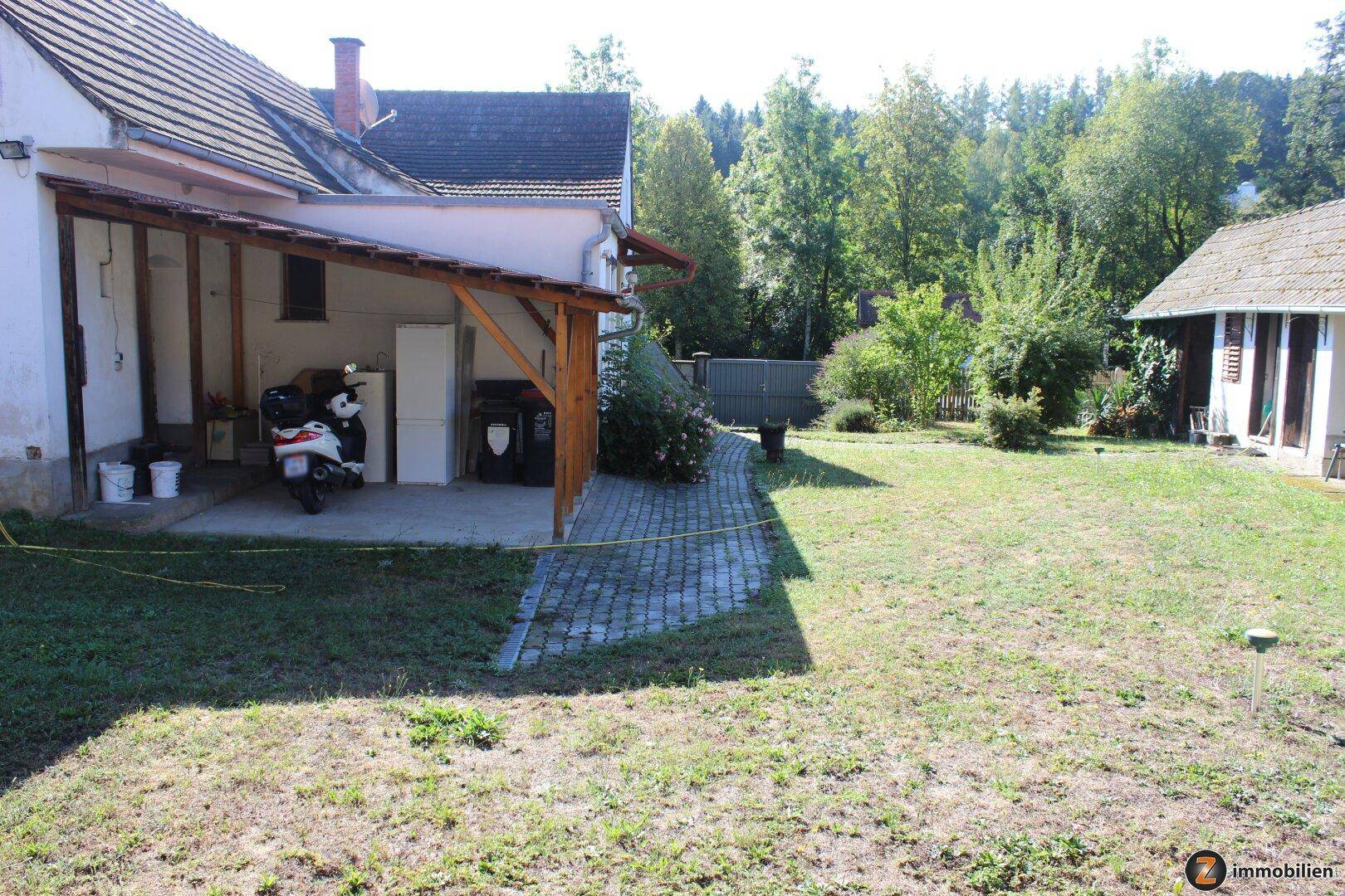 Gartenbereich neben dem Haus mit überdachtem Unterstand und Rasenfläche.