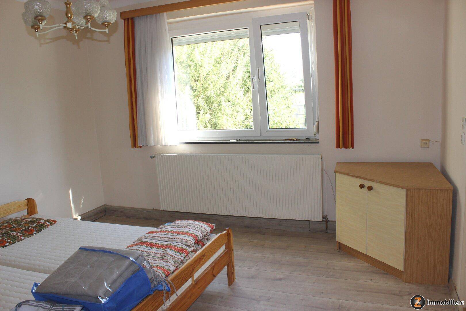 Schlafzimmer mit Doppelbett, Laminatboden und Fenster mit Blick ins Grüne.