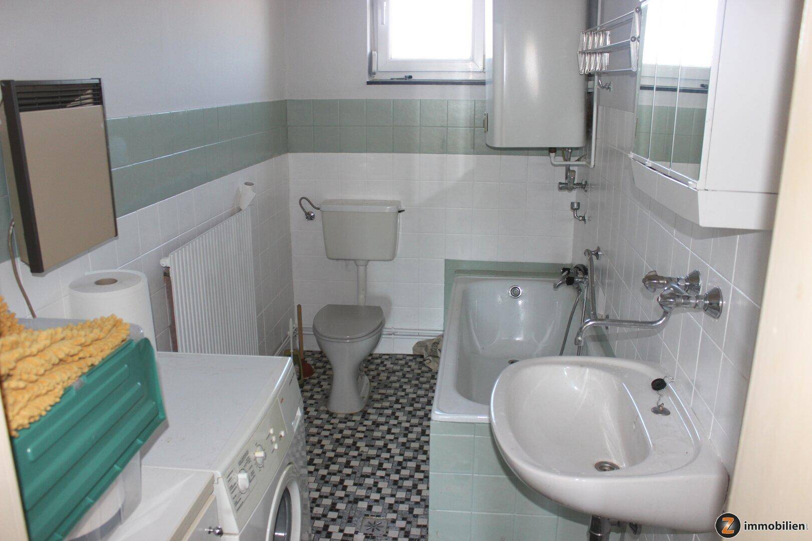 Badezimmer mit Badewanne, WC, Waschmaschine und Fenster.