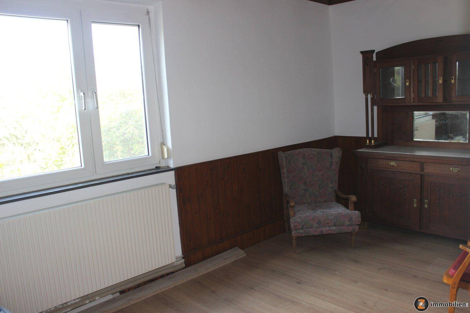 Helles Wohnzimmer mit Holztäfelung, Laminatboden und großem Fenster.