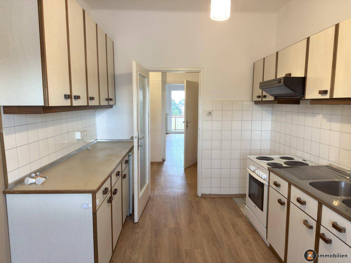 Funktionale Küche mit älteren Einbauschränken und Blick in den angrenzenden Wohnbereich.