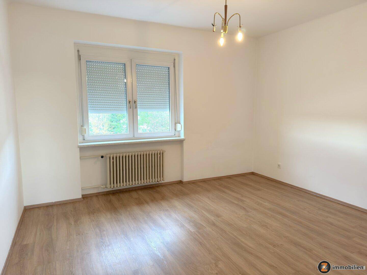 Ruhiges Schlafzimmer mit Laminatboden, Fenster und Heizkörper, ideal für erholsame Nächte.