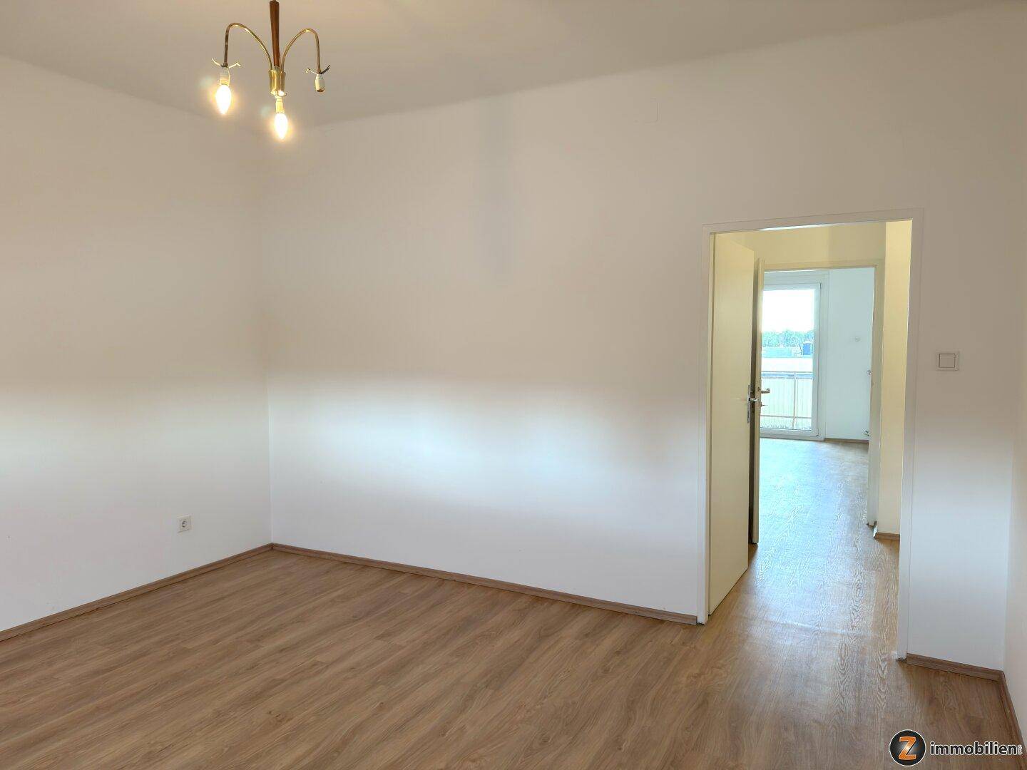 Geräumiges Schlafzimmer mit Laminatboden und Zugang zu einem hellen Nebenraum mit Balkon.