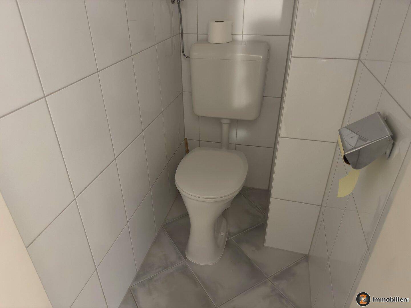 Separates WC mit Toilette und hellen Fliesen an Wänden und Boden.