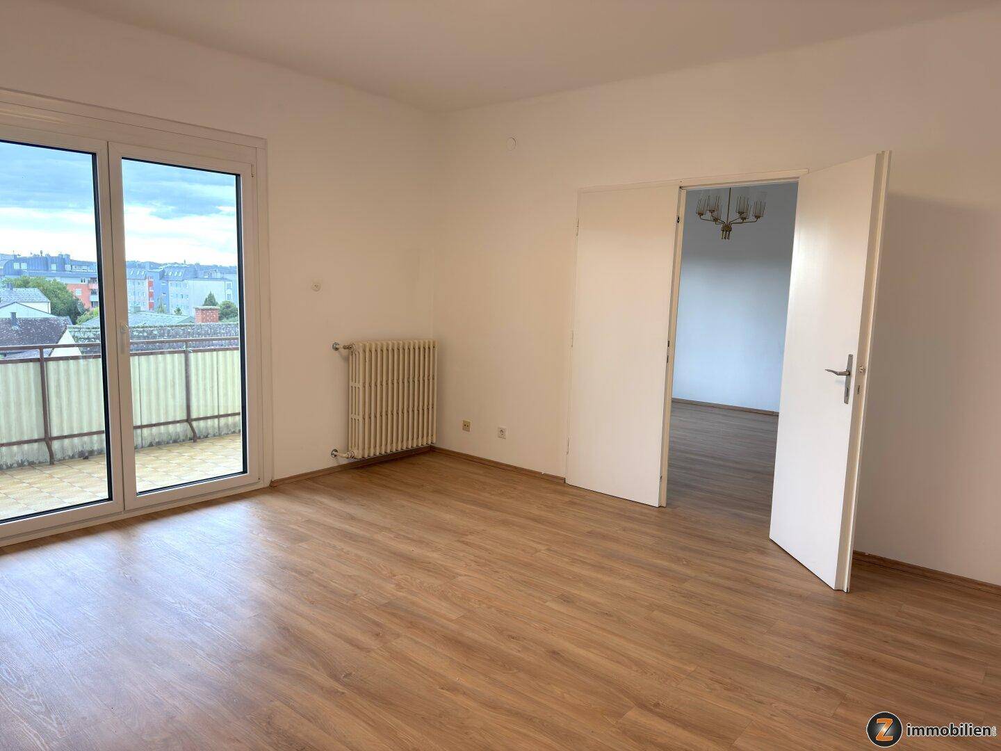 Helles Wohnzimmer mit Laminatboden und Zugang zu einem Balkon oder einer Terrasse.