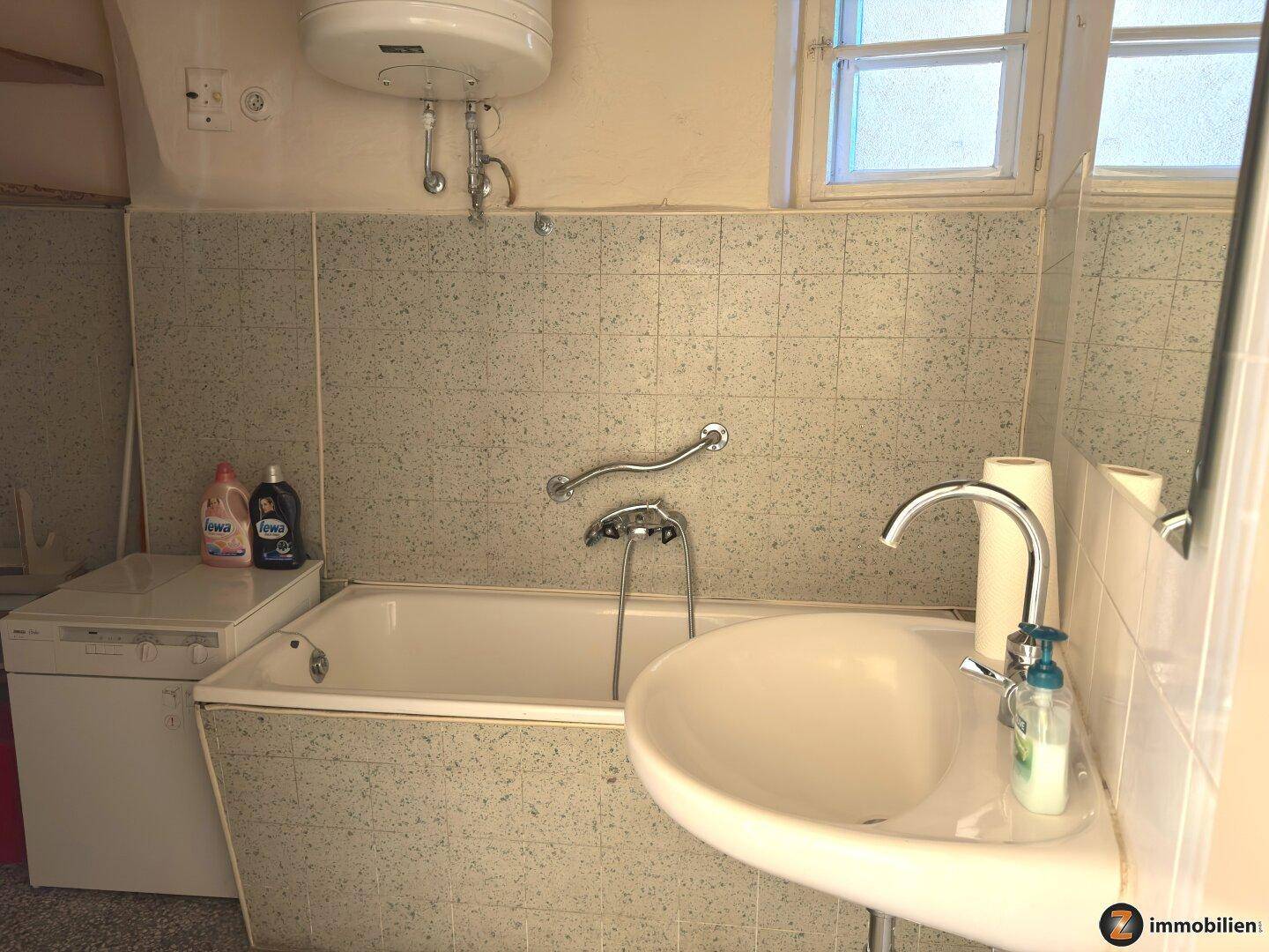 Badezimmer mit Badewanne, Waschbecken und Fliesen, sowie einem Fenster für Tageslicht.